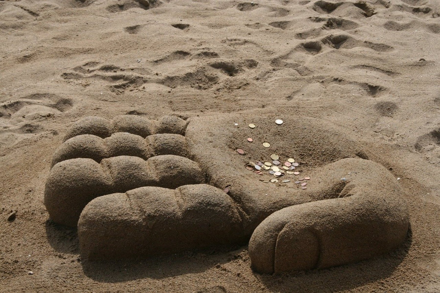 En strand med ett sandslott som liknar en hand. På handen ligger det mynt