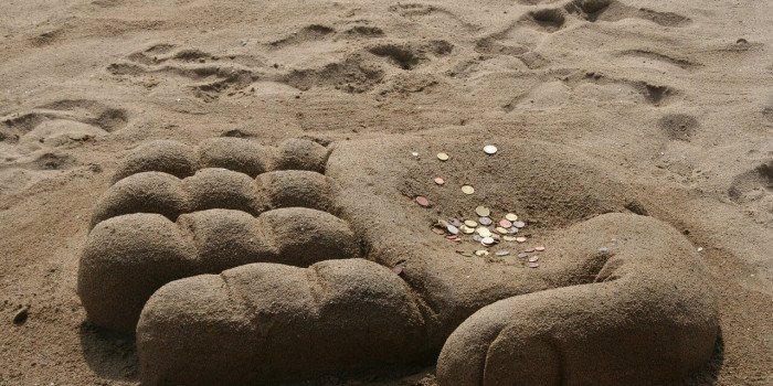 En strand med ett sandslott som liknar en hand. På handen ligger det mynt