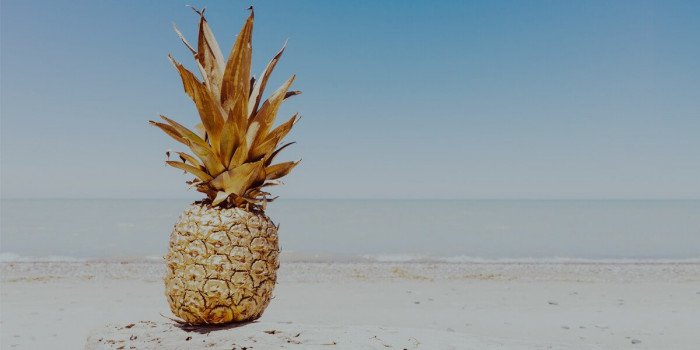 En guldig ananas på en solig sandstrand med vågor i bakgrunden