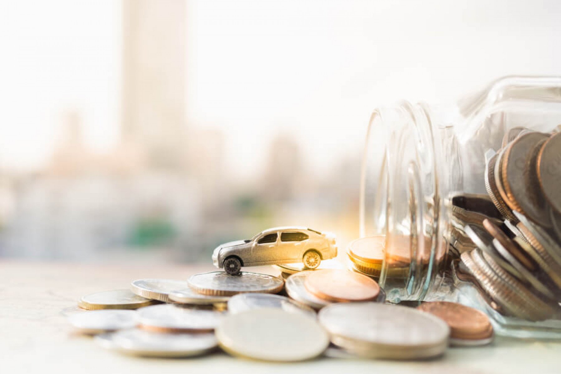 En glasburk ligger på ett bord med mynt ligger uthällda på ett bord. Ut ur glasburken kommer en leksaksbil
