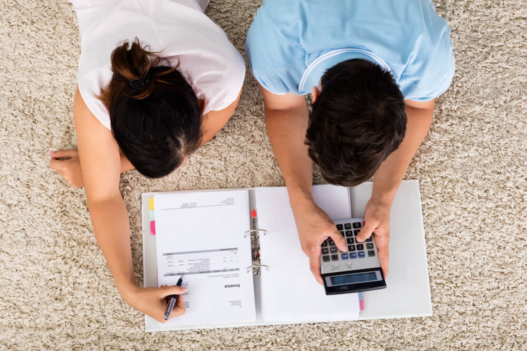 Två personer ligger ned på en matta med fakturor och en miniräknare