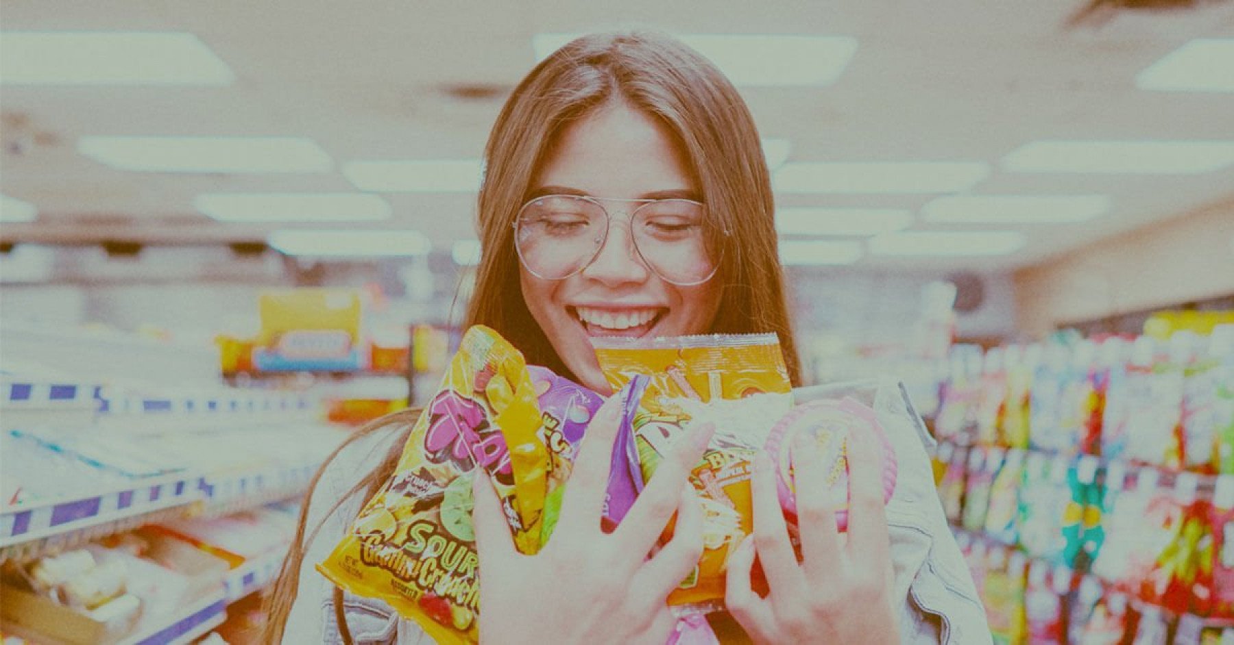 En ungdom står i en kiosk och håller i ett gäng godispåsar i sin famn